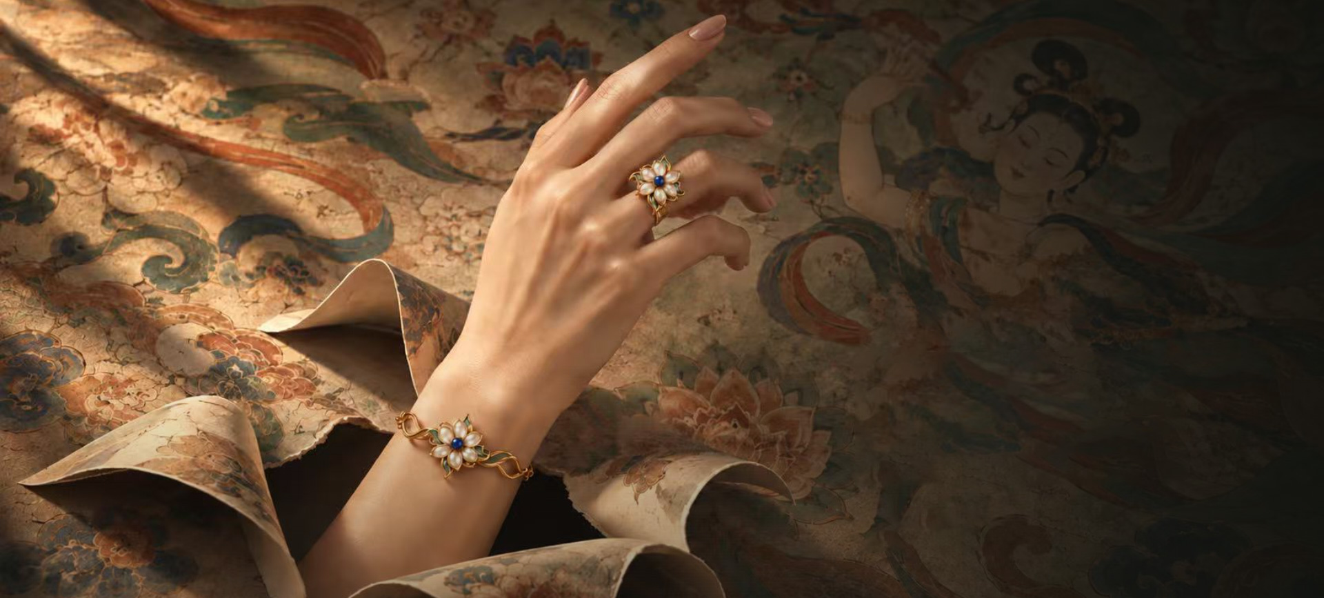 A hand resting against a painted Dunhuang mural, wearing the Lotus Ring and the Lotus Bracelet.